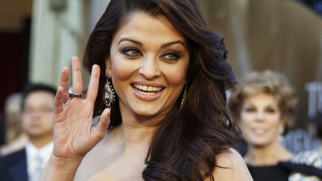 Aishwarya Rai smiling and waving with glamorous earrings and flowing hair wallpaper background