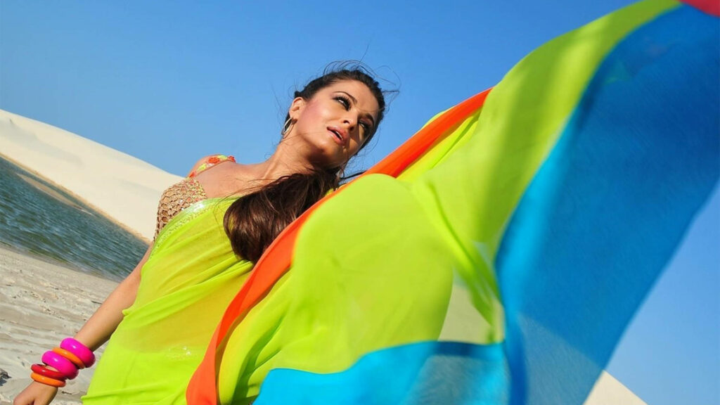 Aishwarya Rai in bright green saree with colorful accents against blue sky and sandy dunes wallpaper