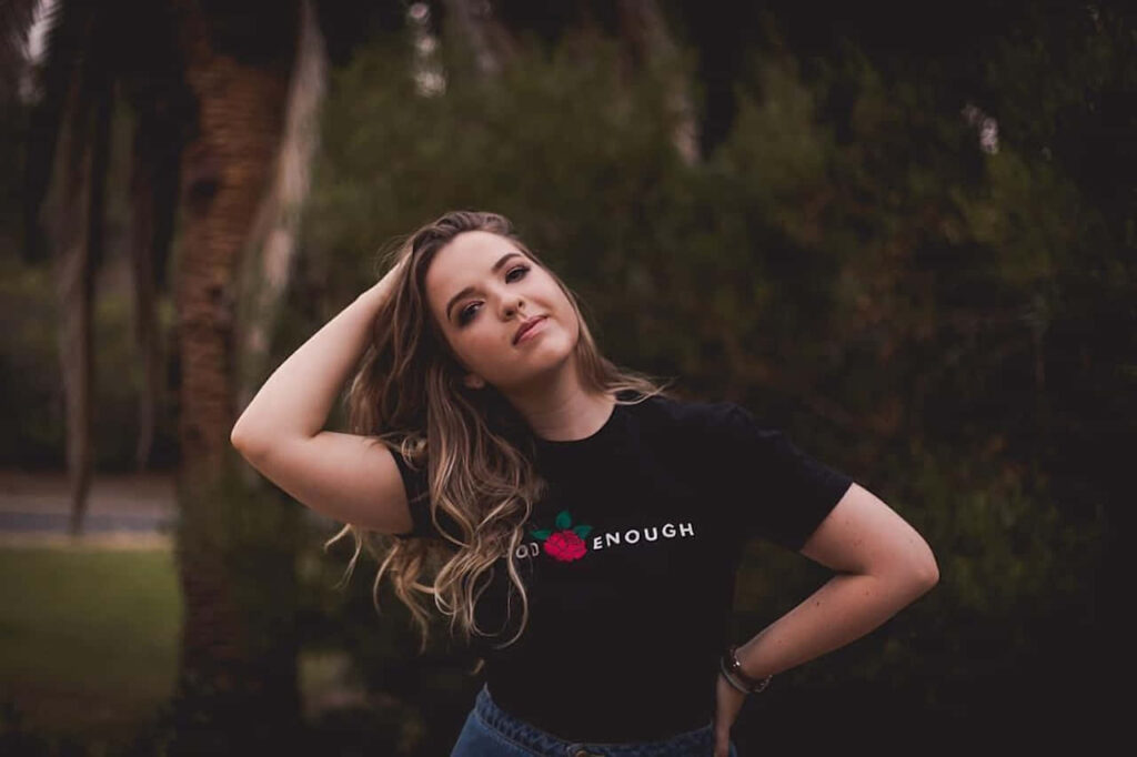 Aislinn Paul in thoughtful pose outdoors surrounded by lush greenery and soft natural light Wallpaper