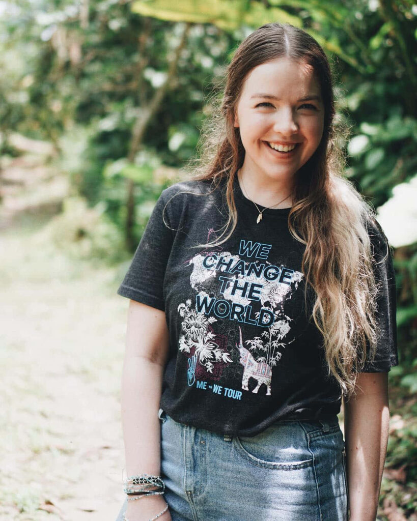 Aislinn Paul smiling outdoors in a positive message t-shirt surrounded by lush green nature background Wallpaper