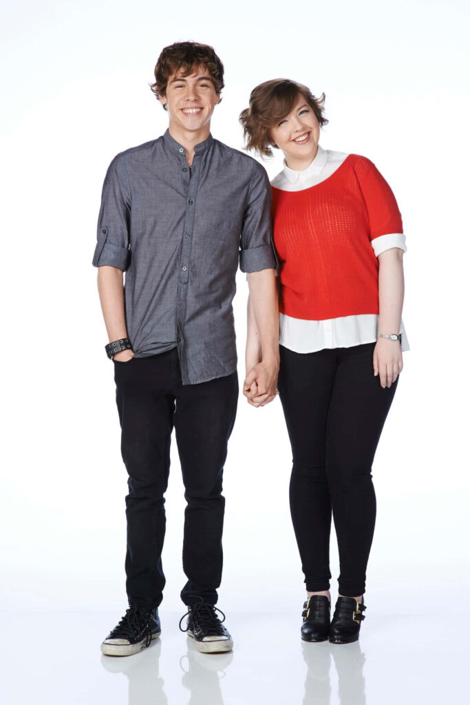 Aislinn Paul smiling warmly in bright studio holding hands creating cheerful friendly wallpaper background