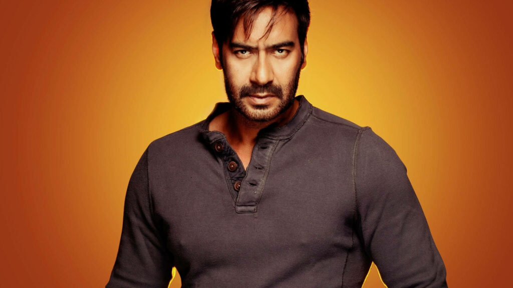 Ajay Devgn confident pose fiery orange background bold intense wallpaper image