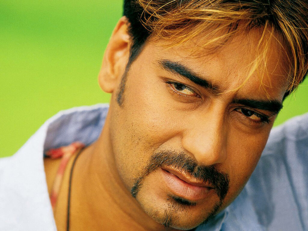 Ajay Devgn close-up portrait with expressive eyes and subtle smile on vibrant green background Wallpaper