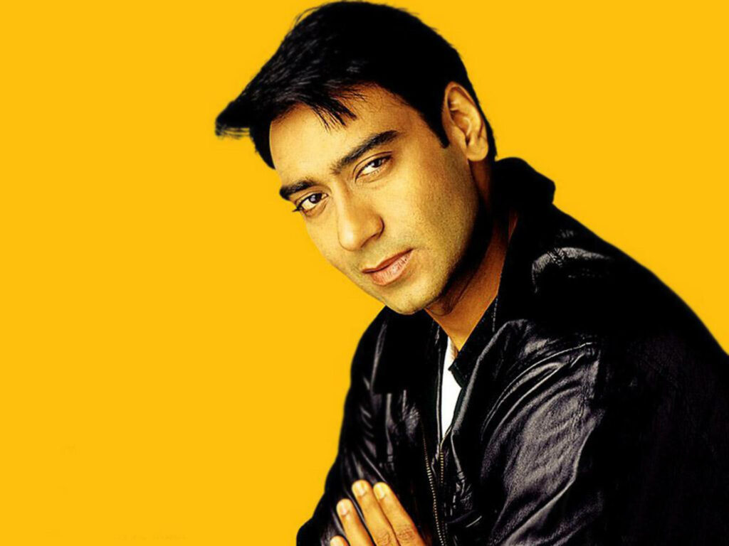 Ajay Devgn confident pose stylish black jacket vibrant yellow modern wallpaper background