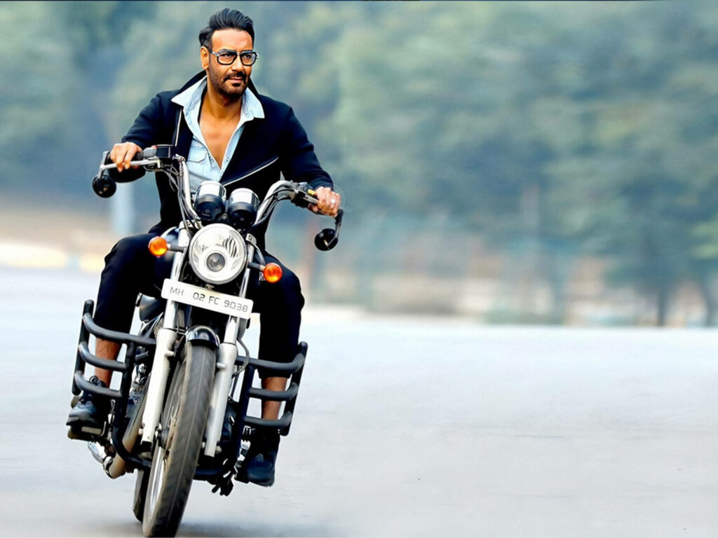 Ajay Devgn in black suit and sunglasses riding motorbike confidently on open road wallpaper
