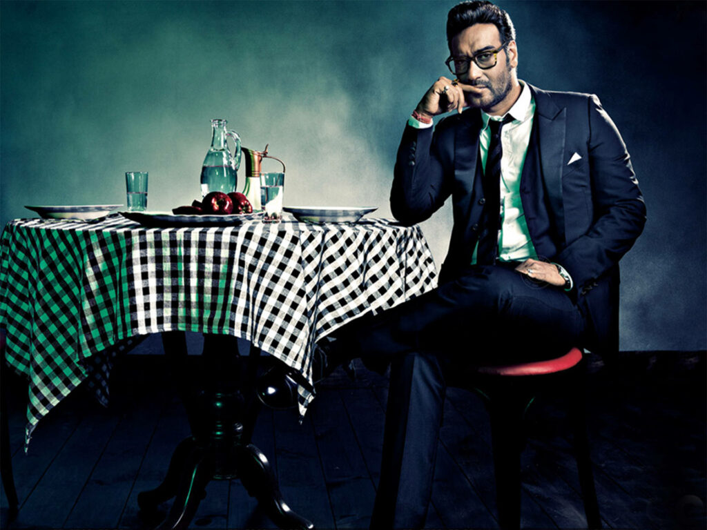 Ajay Devgn in sharp tuxedo sitting confidently at checkered table stylish GQ wallpaper background