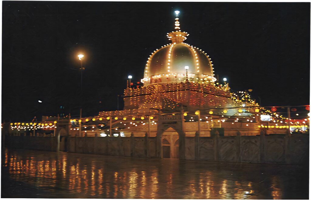 Illuminated Ajmer Dargah Shareef at night with golden lights reflecting on wet ground wallpaper