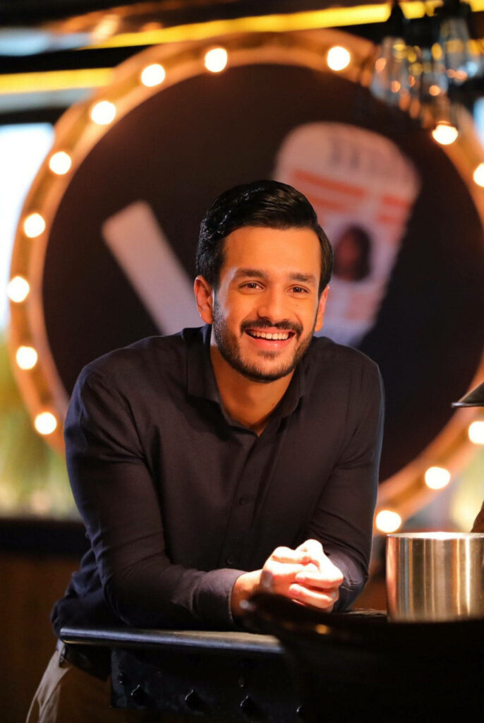 Akhil Akkineni smiling warmly seated with softly lit vibrant wallpaper background