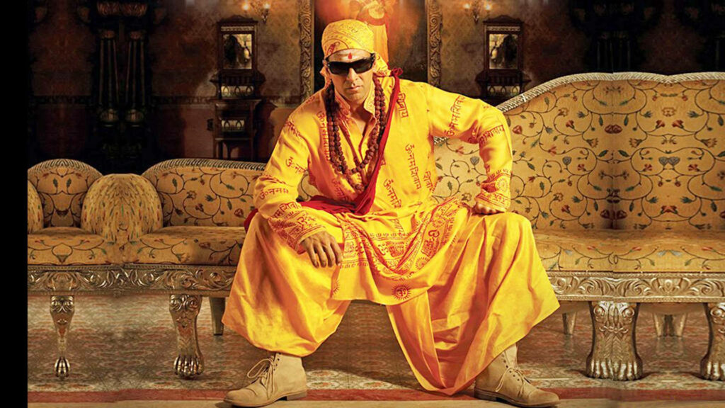 Akshay Kumar in vibrant yellow Indian outfit seated on ornate sofa with wallpaper background