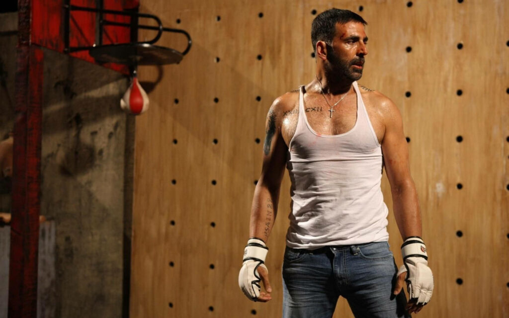 Akshay Kumar in white tank top and boxing gloves confidently training in gym with wooden wall background Wallpaper
