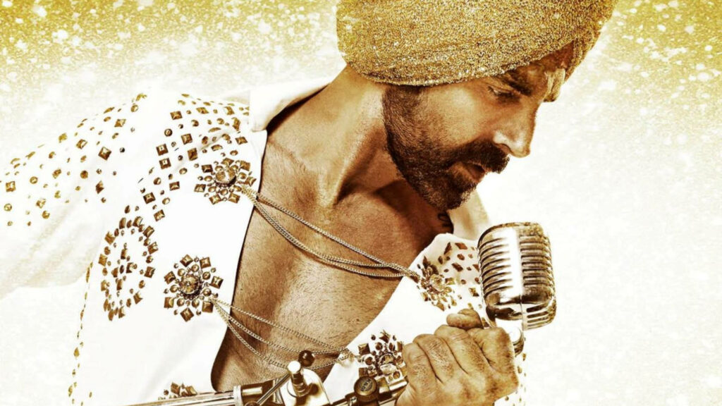 Akshay Kumar singing passionately in sparkling turban and embellished outfit golden backdrop Wallpaper