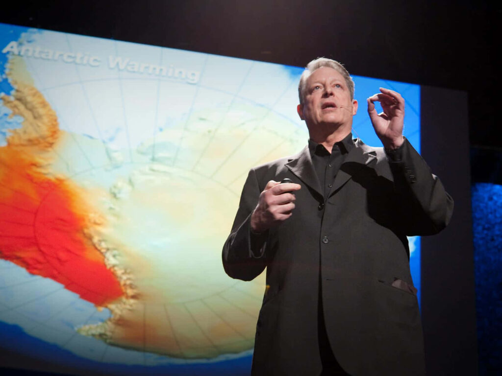 Al Gore speaking on stage about urgent Antarctic warming with climate change visuals behind him Wallpaper