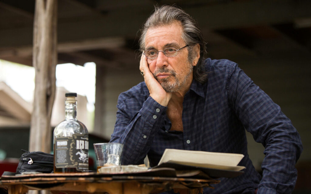Al Pacino as AJ Manglehorn sitting pensively at rustic table with papers and bottle outdoors Wallpaper