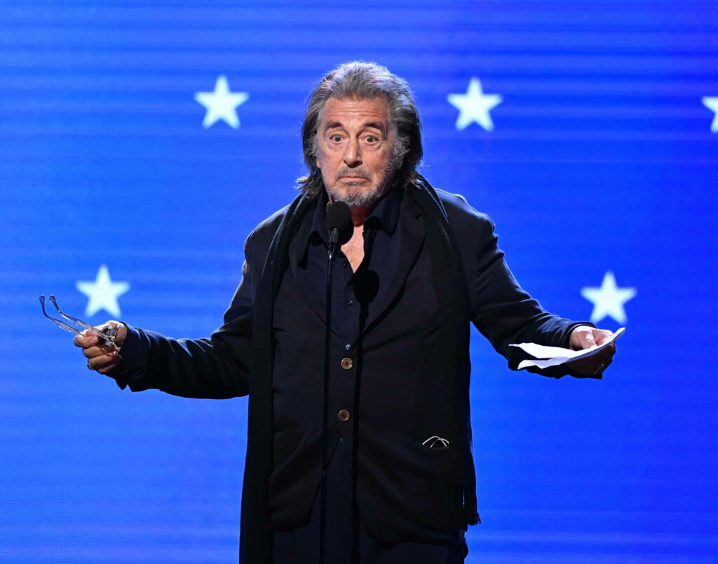 Al Pacino on stage at Critics Choice Awards blue star backdrop holding glasses and paper Wallpaper