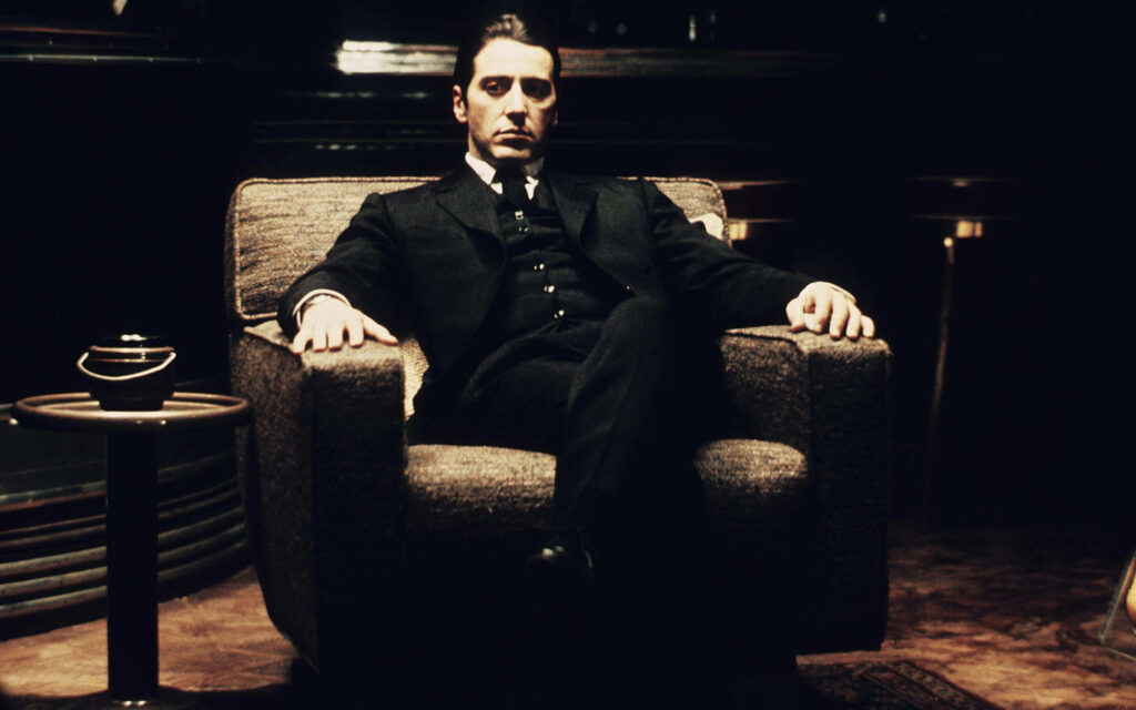 Al Pacino as Michael Corleone sitting confidently in dimly lit room powerful presence wallpaper