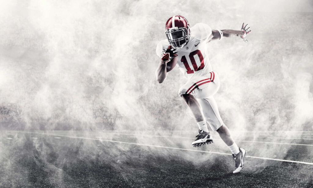 Alabama Crimson Tide football player in full uniform bursts through smoke showcasing intensity Wallpaper