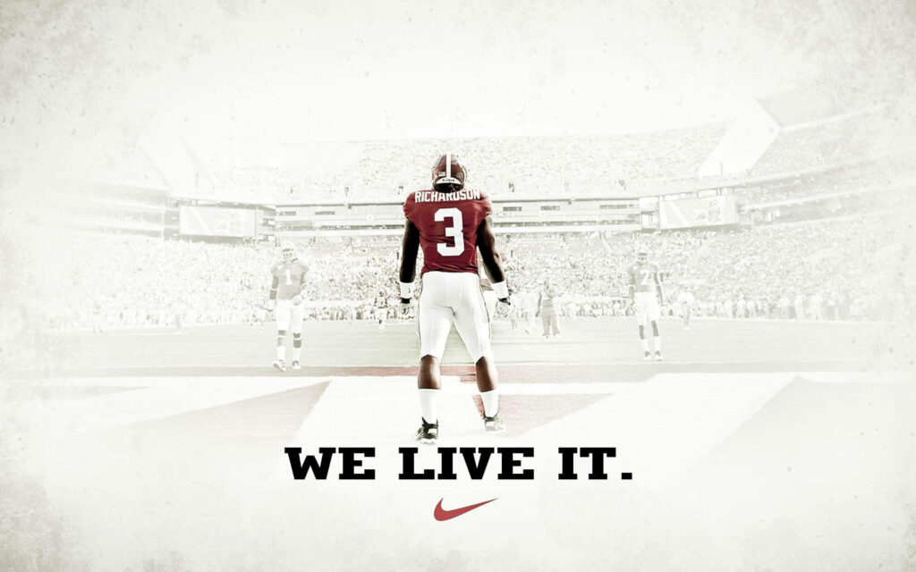 Alabama Crimson Tide football player on field with packed stadium and WE LIVE IT Nike wallpaper