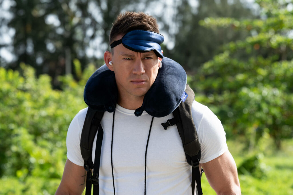 Alan from The Lost City exploring dense jungle wearing white t-shirt travel neck pillow backpack background Wallpaper