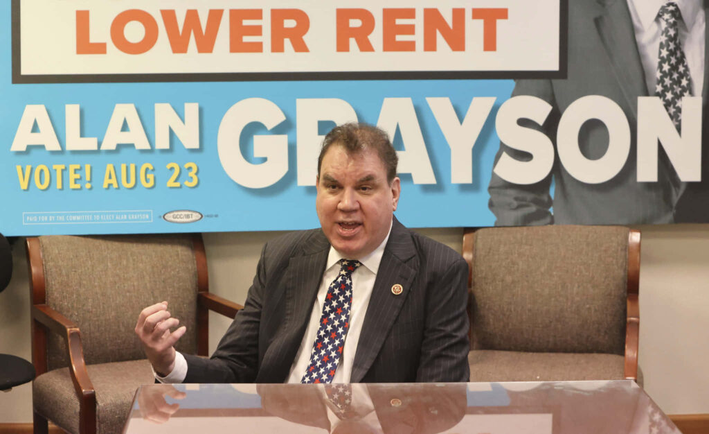 Alan Grayson speaking at campaign event promoting rent reduction with name in background wallpaper