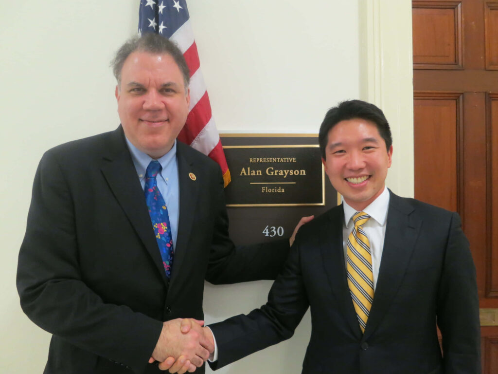 Alan Grayson congratulates smiling Asian man with handshake outside office sign celebrating success Wallpaper