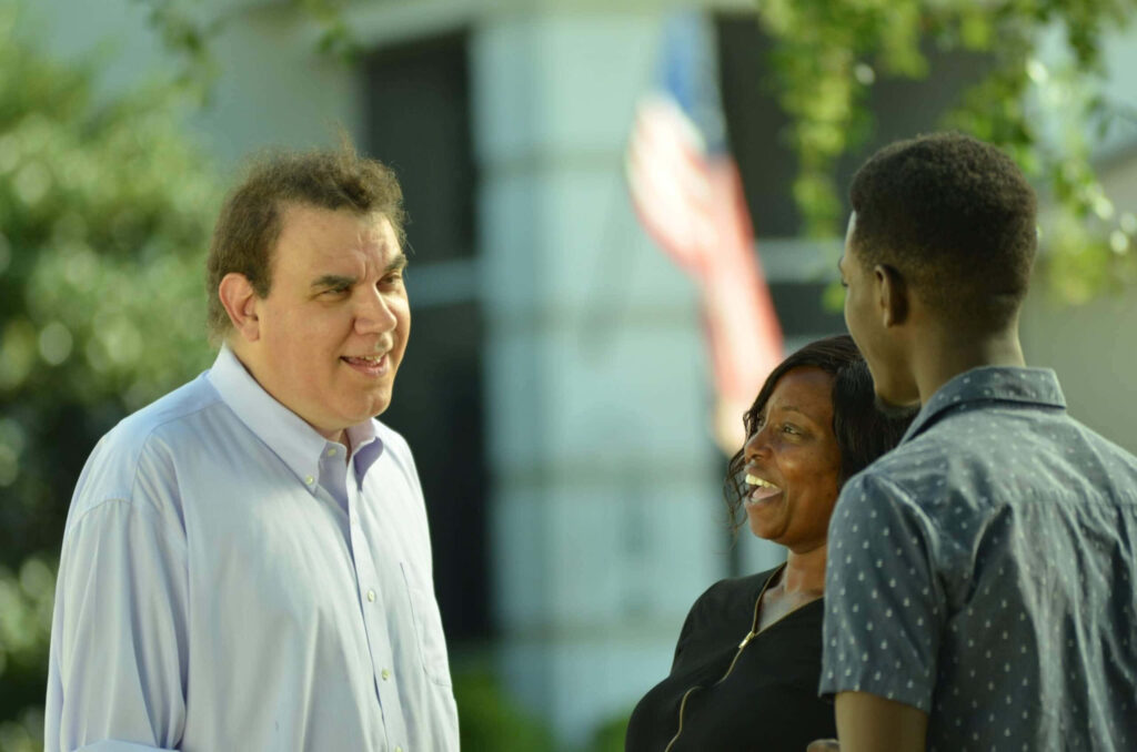 Alan Grayson American politician engaging warmly with community outdoors on wallpaper background