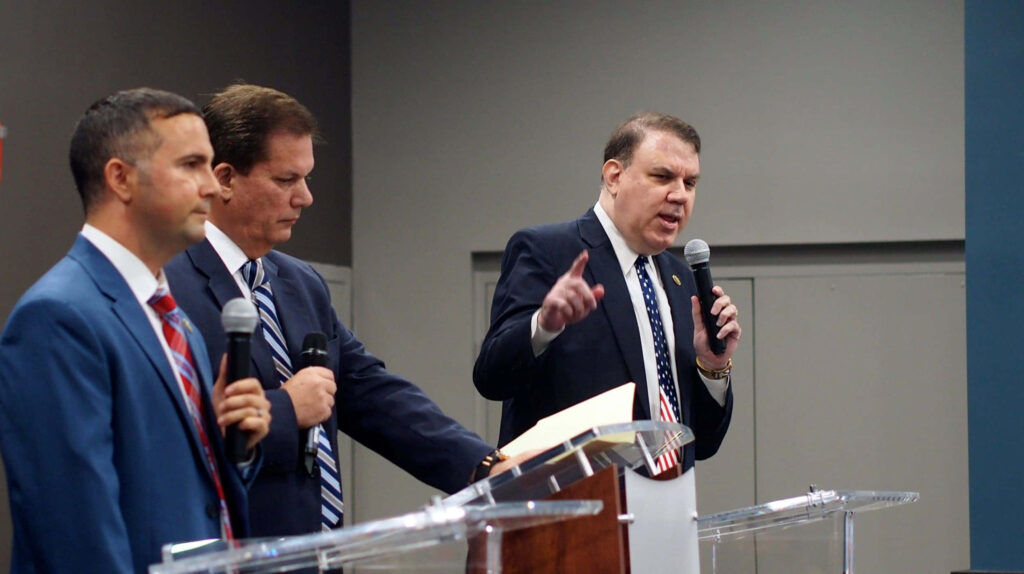 Alan Grayson passionately speaking at podium during formal political debate with other candidates Wallpaper
