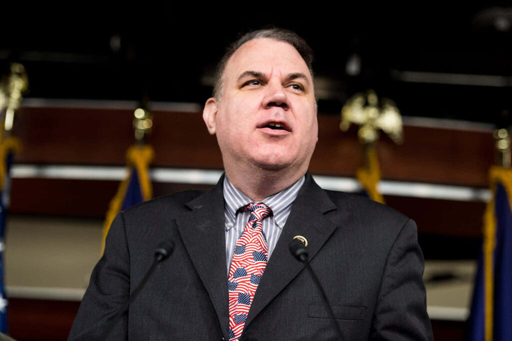 Alan Grayson speaking at a patriotic event with American flags and formal decor background wallpaper