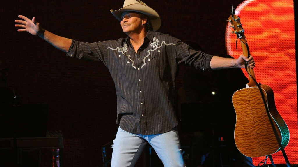 Alan Jackson on stage with cowboy hat holding guitar arms open wide lively concert scene Wallpaper