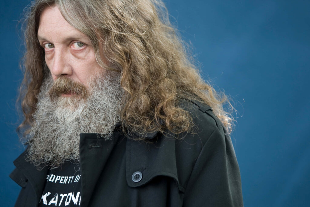 Alan Moore portrait with intense gaze long hair and beard blue background graphic novel writer Wallpaper