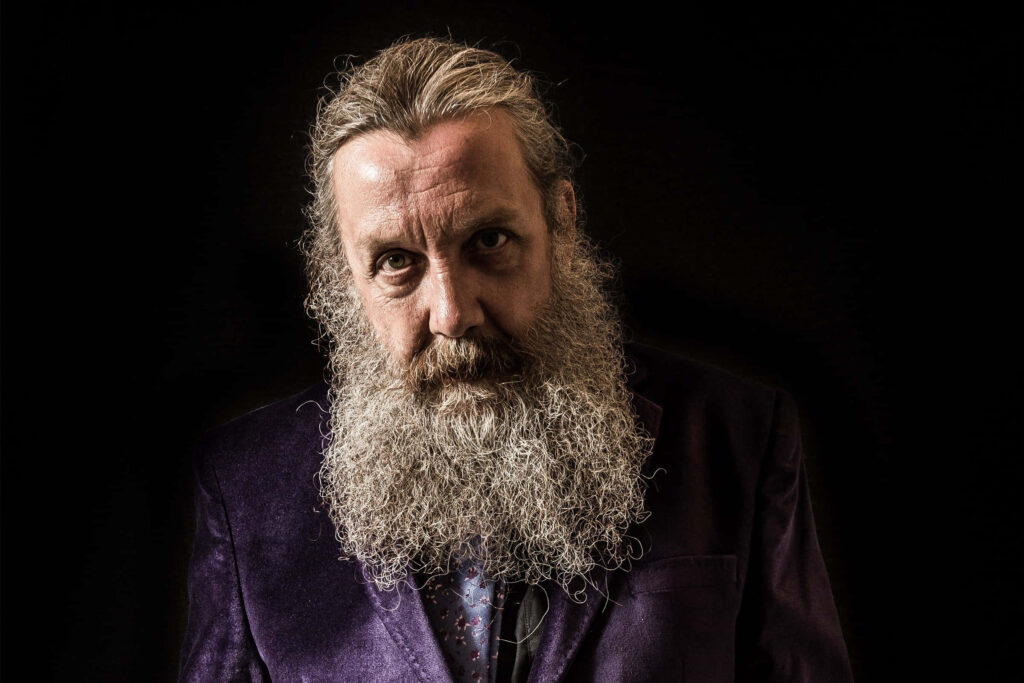 Portrait of Alan Moore with long beard intense gaze dark background creative writer wallpaper