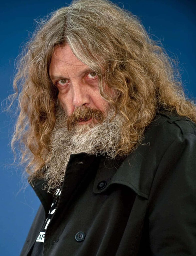 Alan Moore portrait with long curly hair dark coat against deep blue background wallpaper