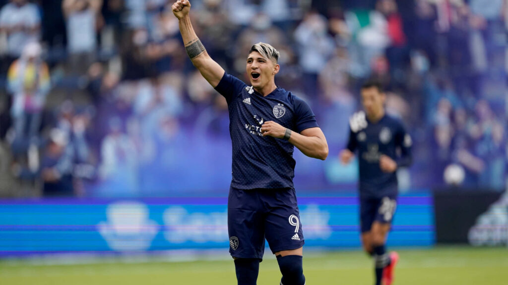 Alan Pulido celebrates victorious goal on field with fist raised and cheering crowd background Wallpaper
