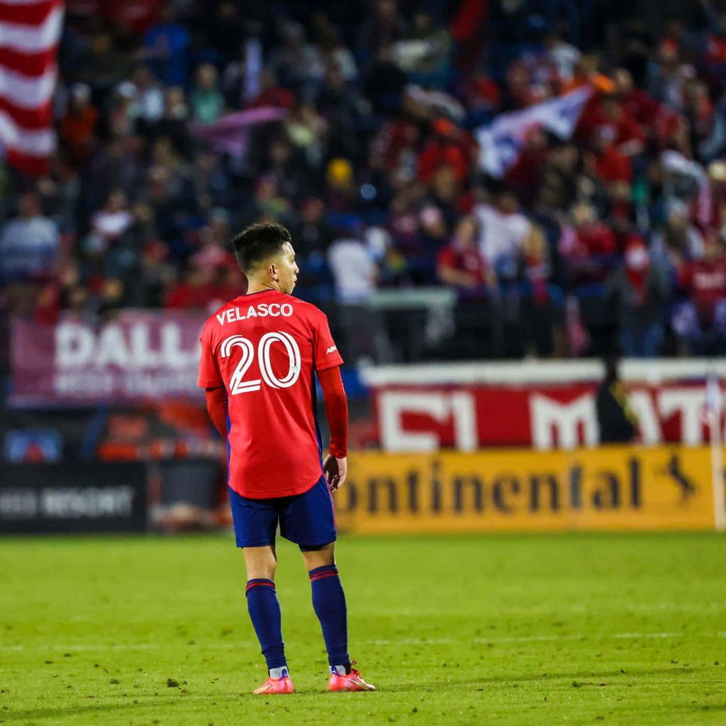 FC Dallas Alan Velasco red jersey number 20 on pitch blurred stadium background wallpaper