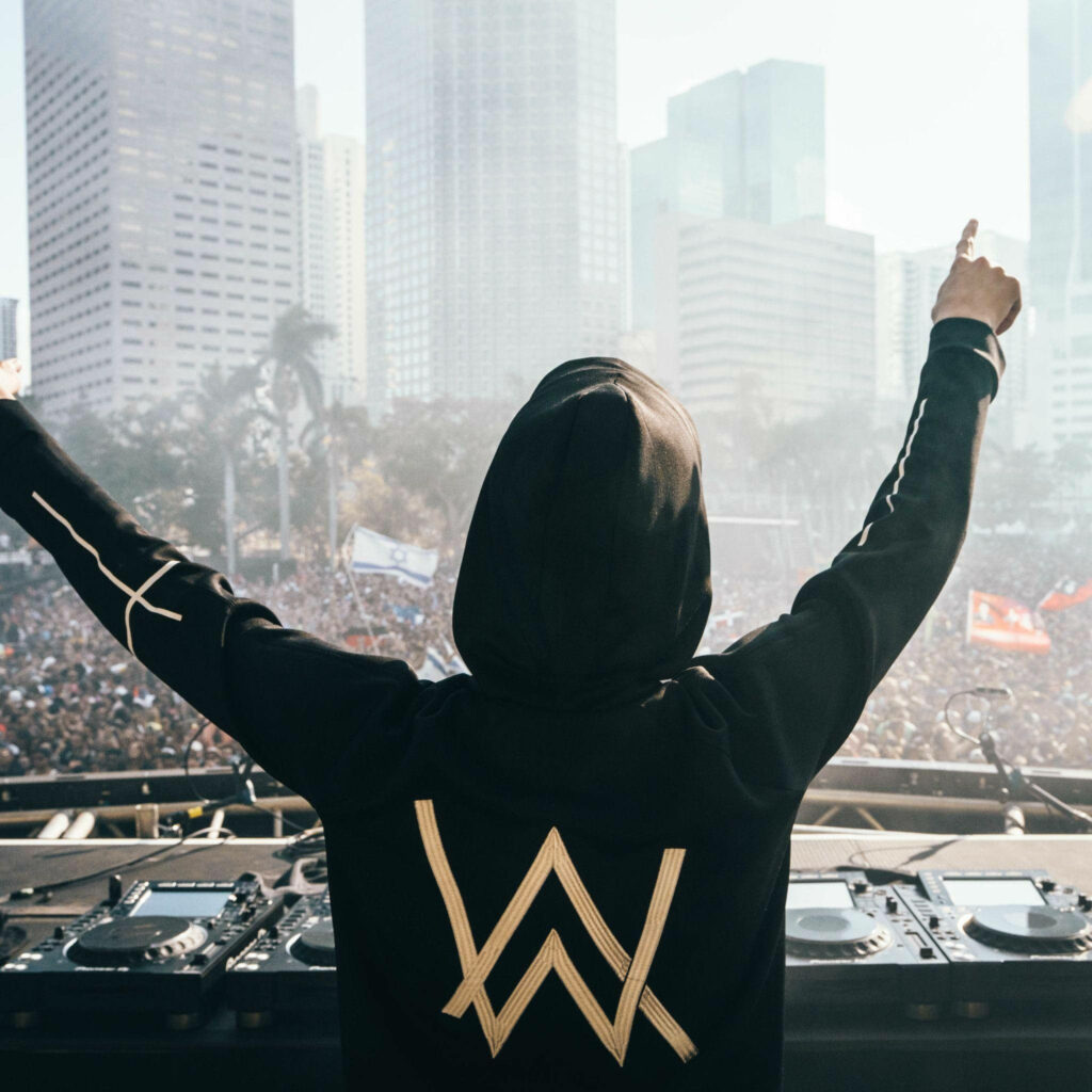 Edgy Alan Walker Captivating a Roaring Audience Amidst Urban Skyscrapers: A Mesmerizing Shot from Behind Wallpaper