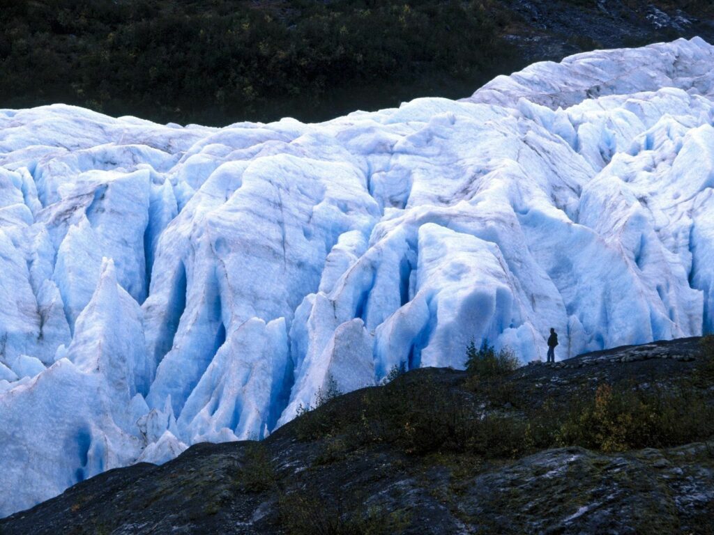 Person standing by massive blue glacier in Alaska rugged icy terrain majestic landscape wallpaper