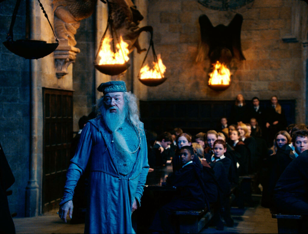 Albus Dumbledore in turquoise robe in Hogwarts Great Hall with students and warm firelight Wallpaper