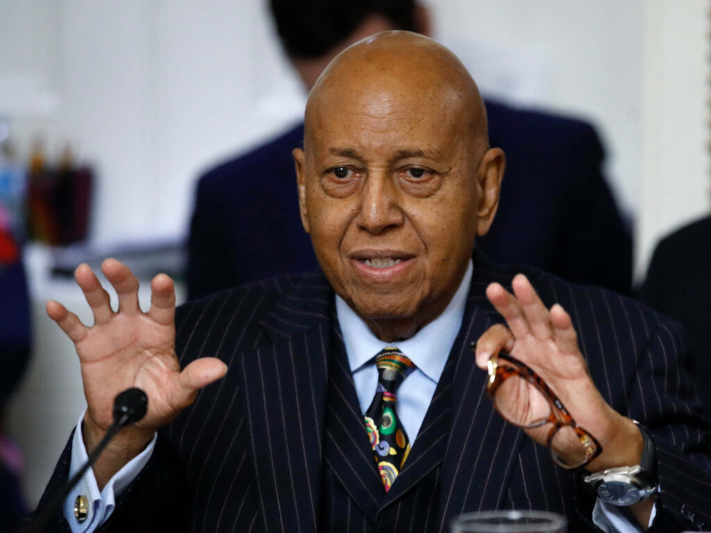 Alcee Hastings seated making expressive hand gestures wearing striped suit colorful tie wallpaper background