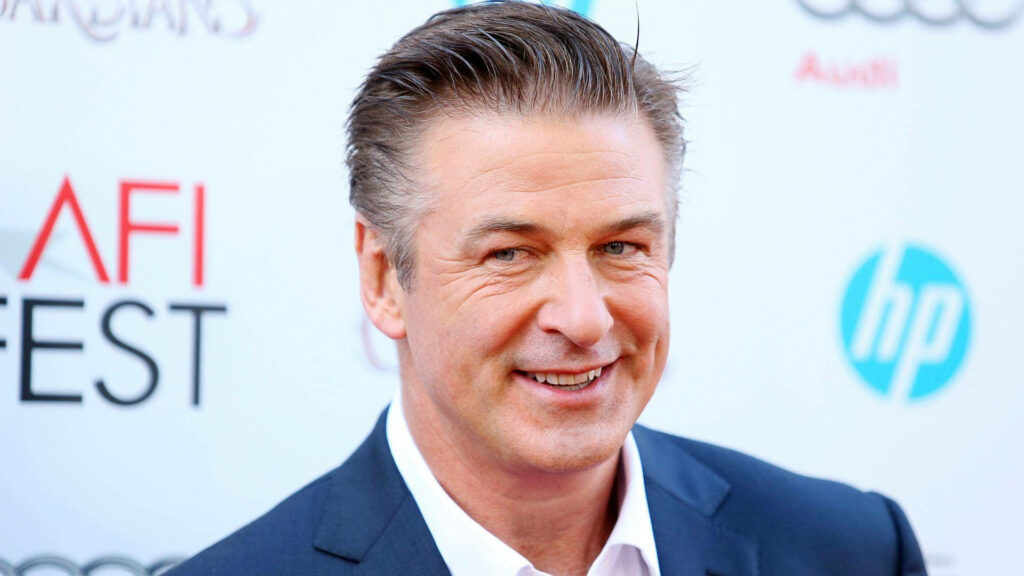 Alec Baldwin smiling in sharp suit at bright event backdrop perfect for sophisticated wallpaper