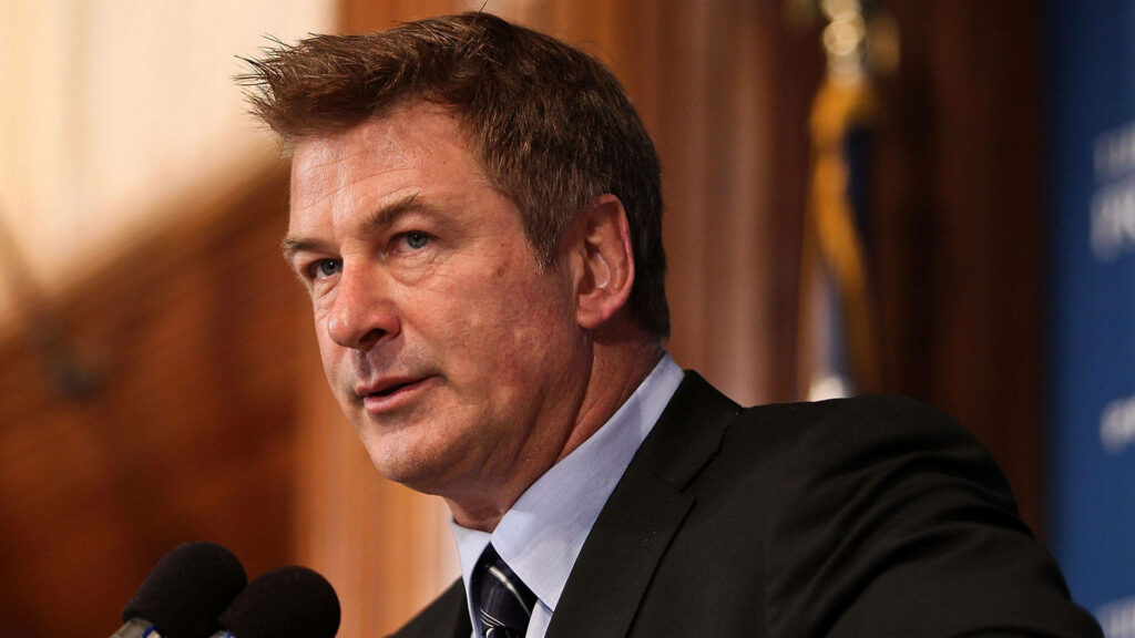 Alec Baldwin in formal attire delivering a powerful speech with elegant intense presence wallpaper