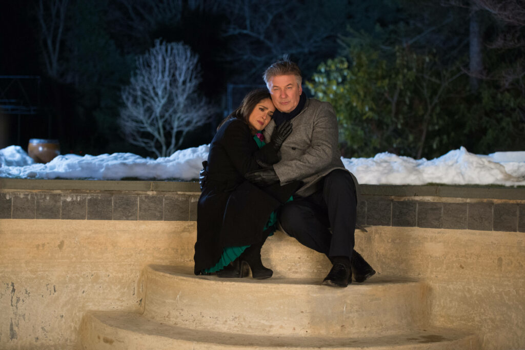 Alec Baldwin warmly embraces woman sitting on outdoor steps in serene winter setting wallpaper