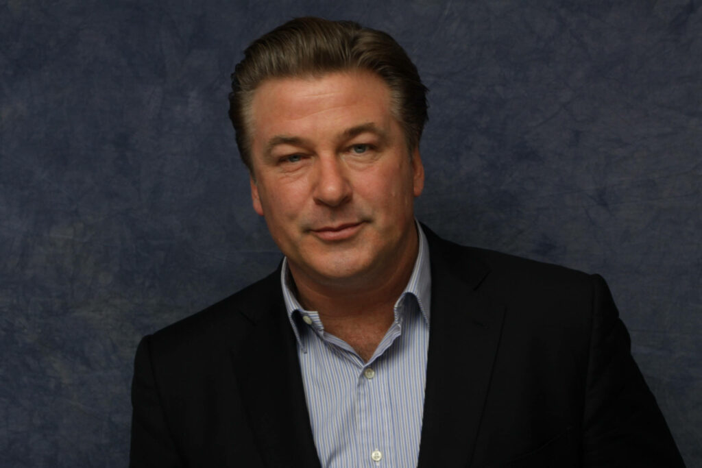 Alec Baldwin confident studio portrait wearing dark suit jacket and striped shirt on blue backdrop Wallpaper