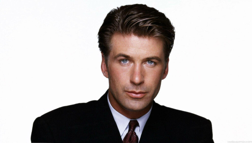 Alec Baldwin in sharp suit with piercing blue eyes on white background confident intense look Wallpaper