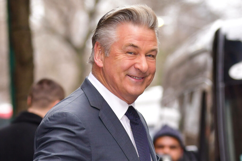 Alec Baldwin smiling outdoors in a formal suit capturing his charismatic presence wallpaper