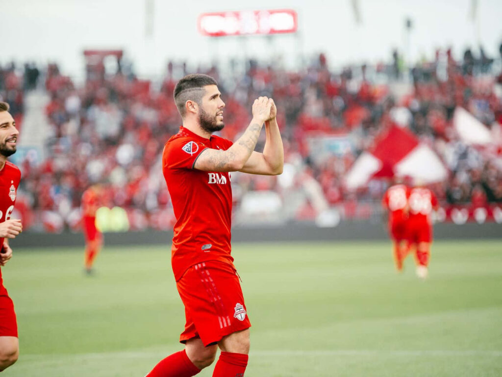 Alejandro Pozuelo celebrating goal in red kit with cheering crowd on football field wallpaper background