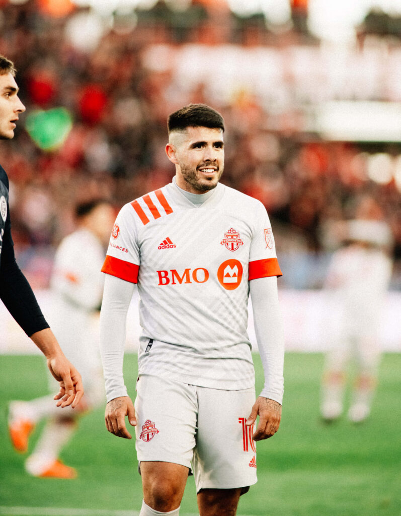 Alejandro Pozuelo in Toronto FC kit amazed during intense match with crowd and teammates visible Wallpaper