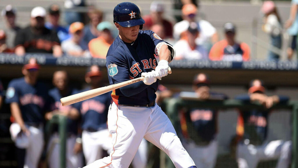 Alex Bregman mid swing in baseball game with teammates and fans in dynamic background wallpaper