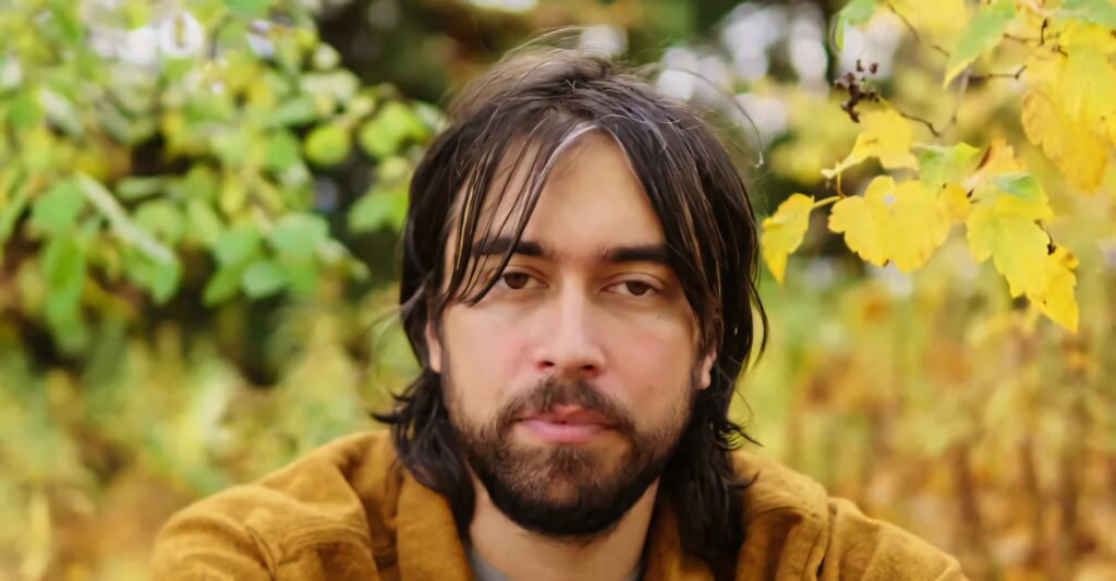 Alex G sitting outdoors with vibrant golden yellow autumn leaves background wallpaper