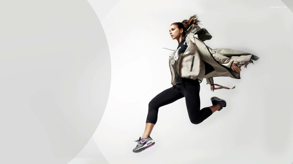 Alex Morgan leaps energetically in white jacket against minimalist background dynamic athleticism Wallpaper