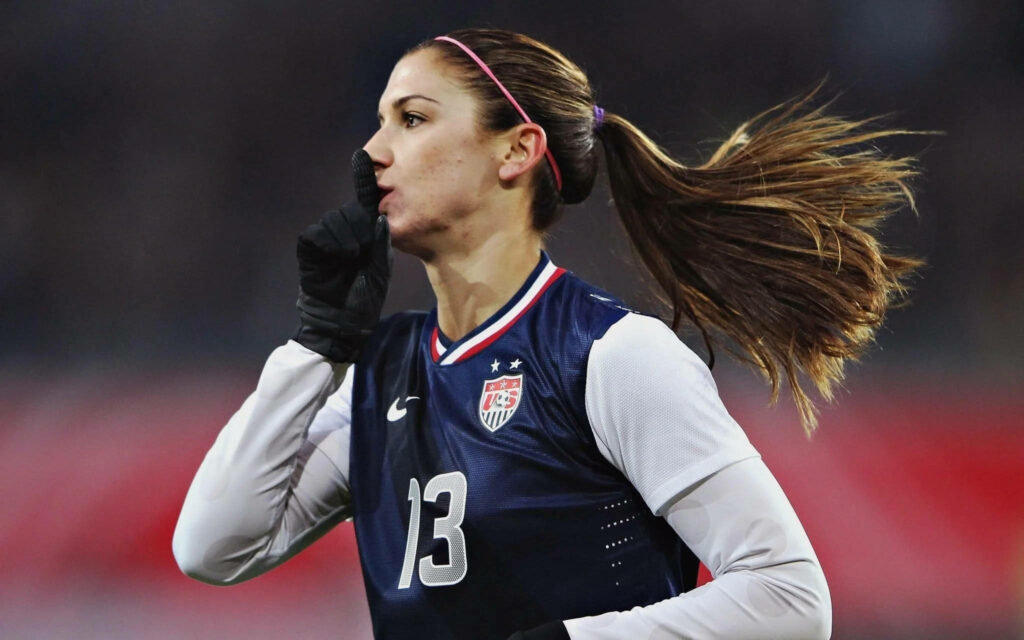 Alex Morgan in USA soccer jersey striking confident focused pose on field wallpaper background