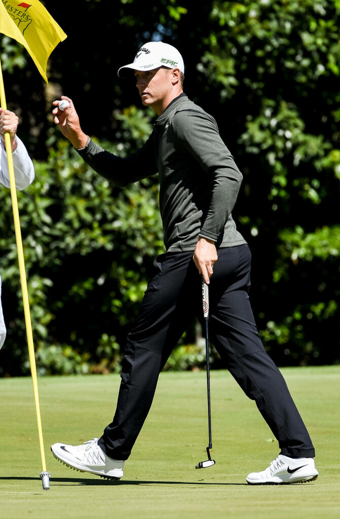 Alex Norén focused on golf course holding golf ball and putter with lush green background Wallpaper